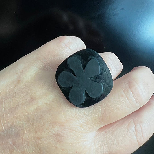 A woman wears a ring topped with a black rubber daisy