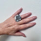 A woman wears a ring topped with a black rubber daisy
