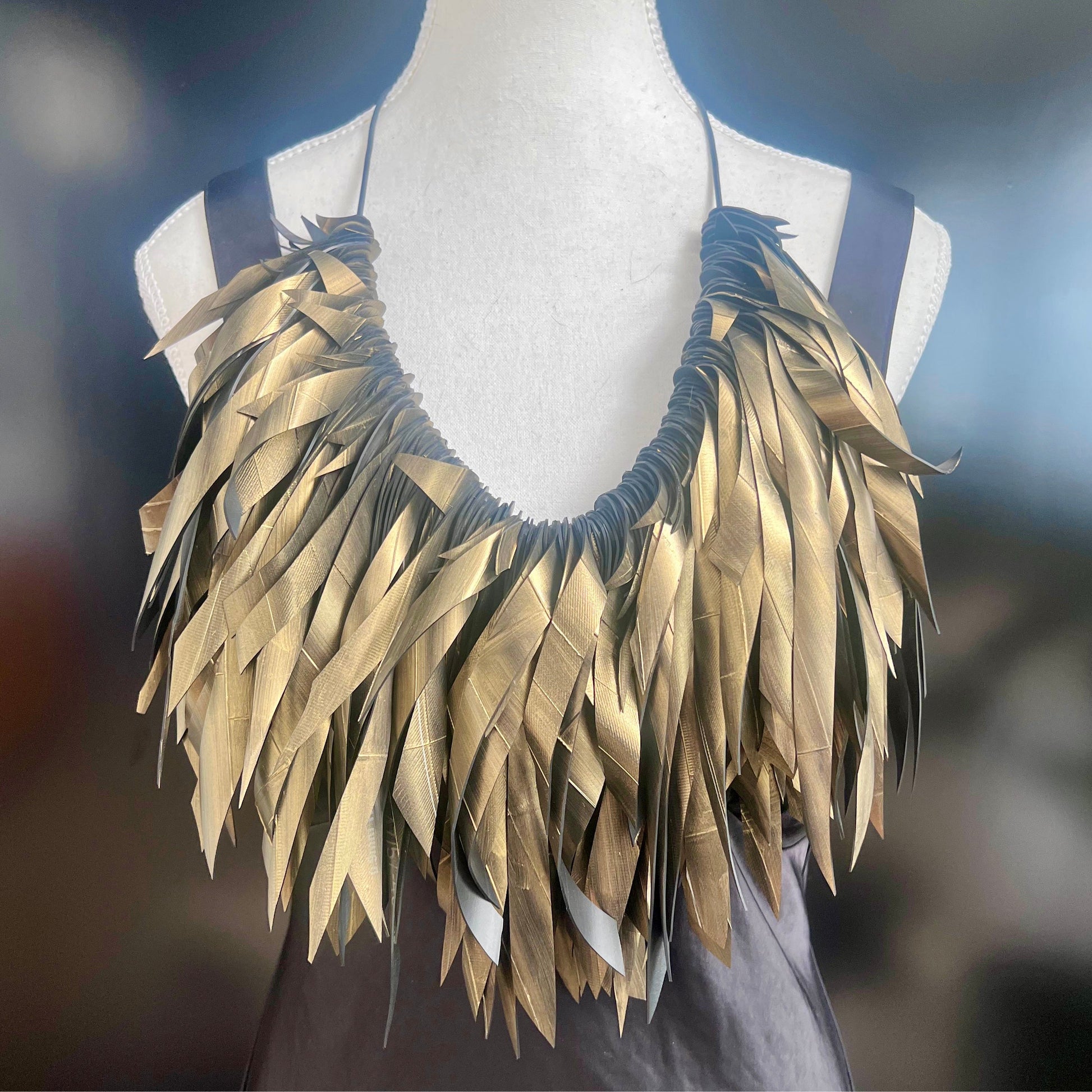 Gold painted recycled rubber necklace on a mannequin against a blurred background