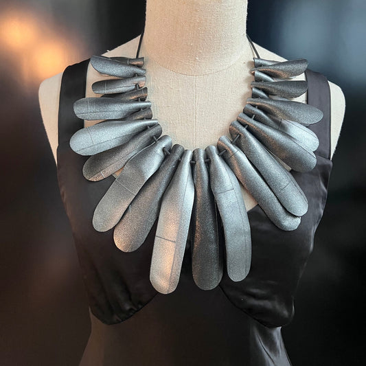A mannequin wearing a large silver rubber necklace
