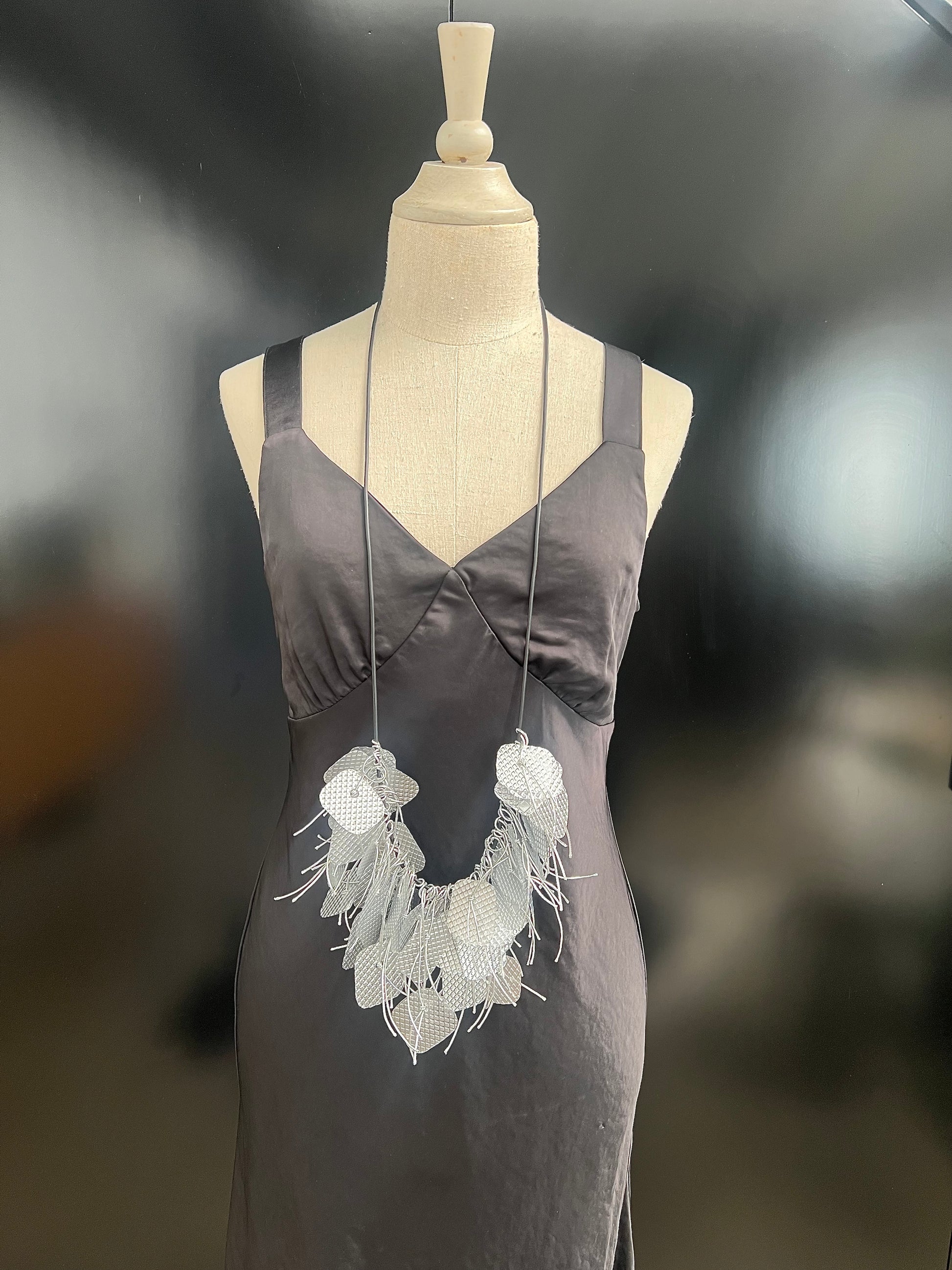 A mannequin wears a long silver tassled necklace