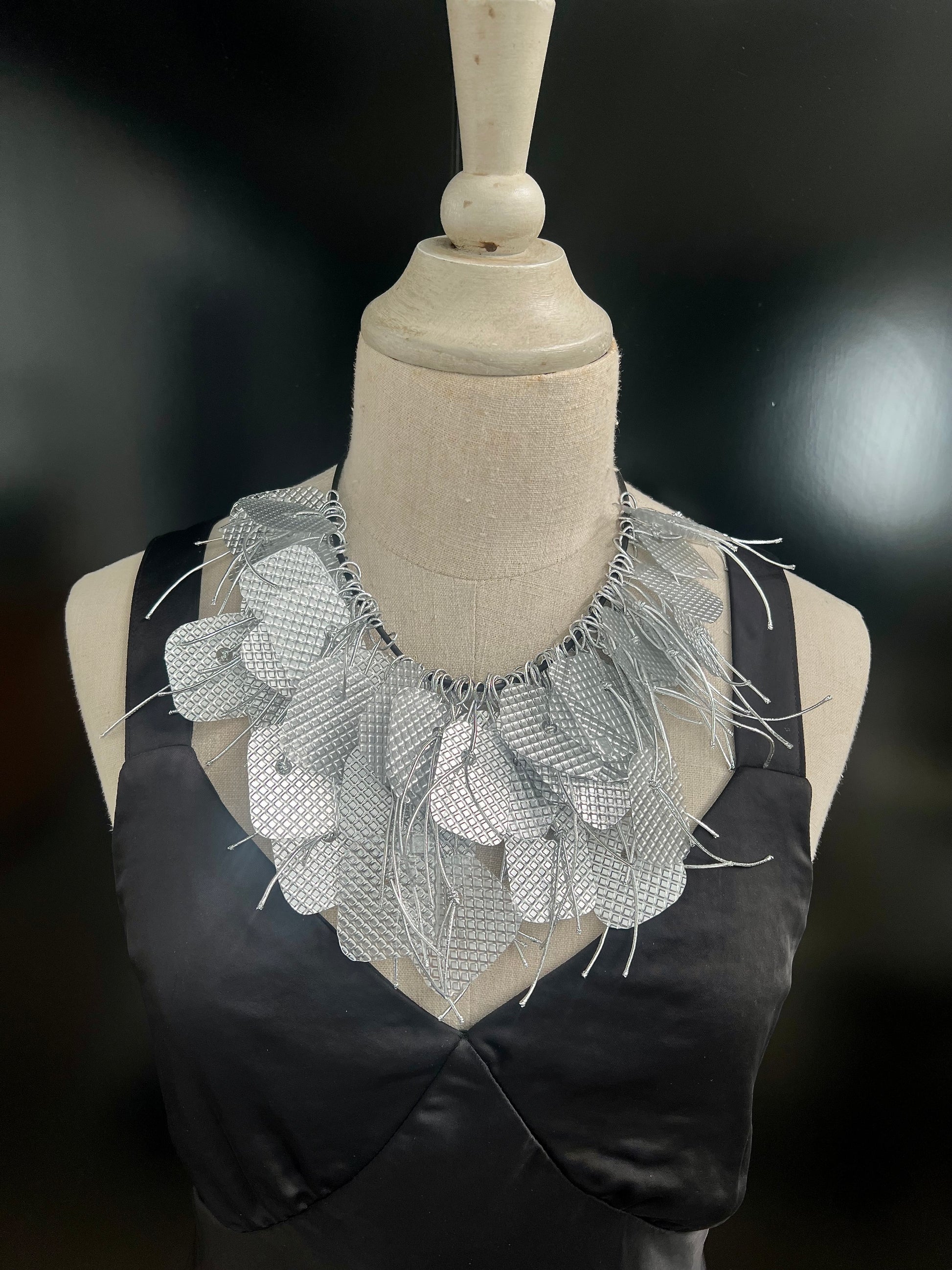 A mannequin wears a large silver tassled plastic necklace