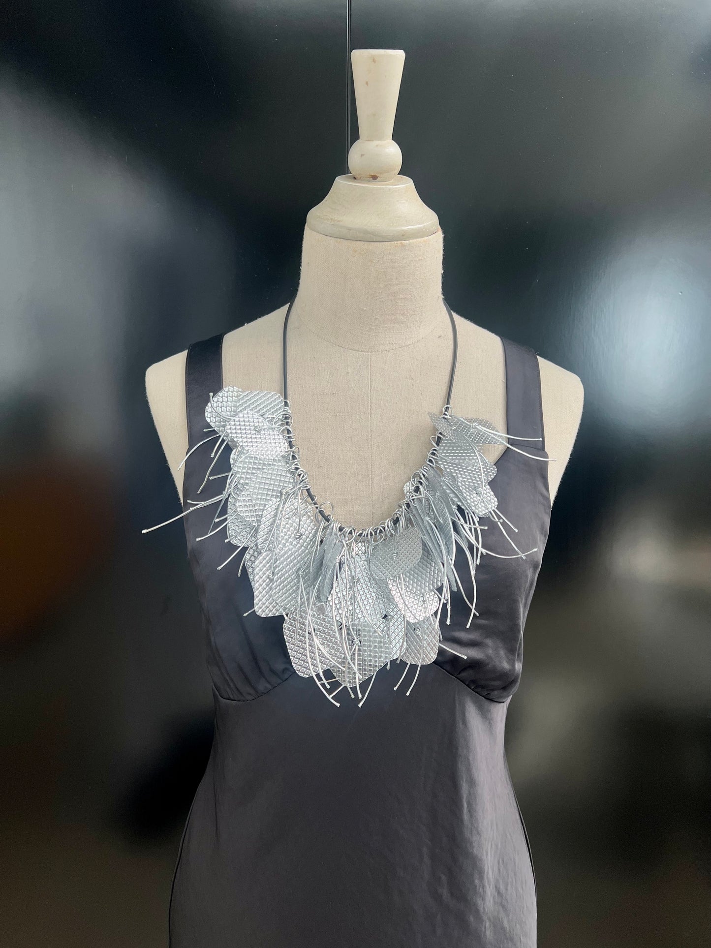A mannequin wears a large silver tassled necklace