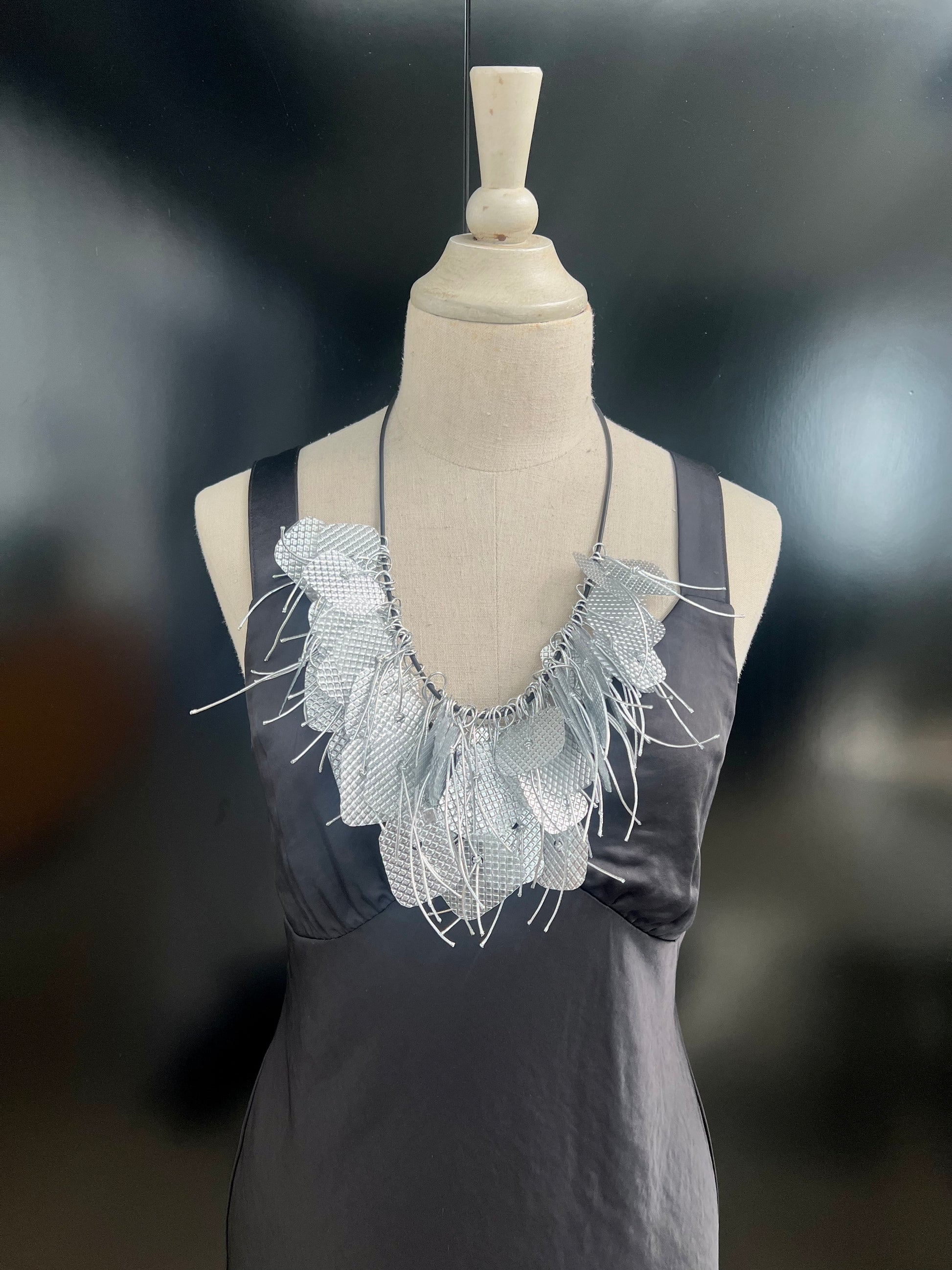 A mannequin wears a large silver tassled necklace