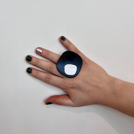 A woman&#39;s hand wears a large organically shaped black and white repurposed rubber and plastics ring