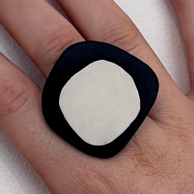 A woman&#39;s finger wears a  statement ring made of black and white repurposed rubber in an organic shape