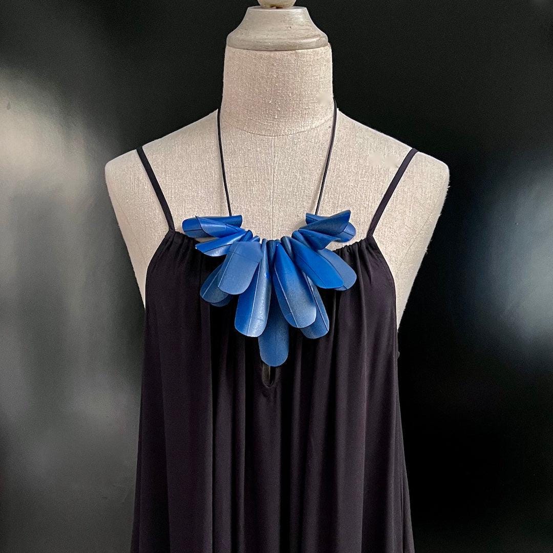 A hand painted blue necklace on a mannequin made from repurposed bicycle inner tubes and resembling a flower