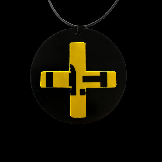 A pendant necklace made from a round rubber disc and a yellow cross cut from advertising plastic