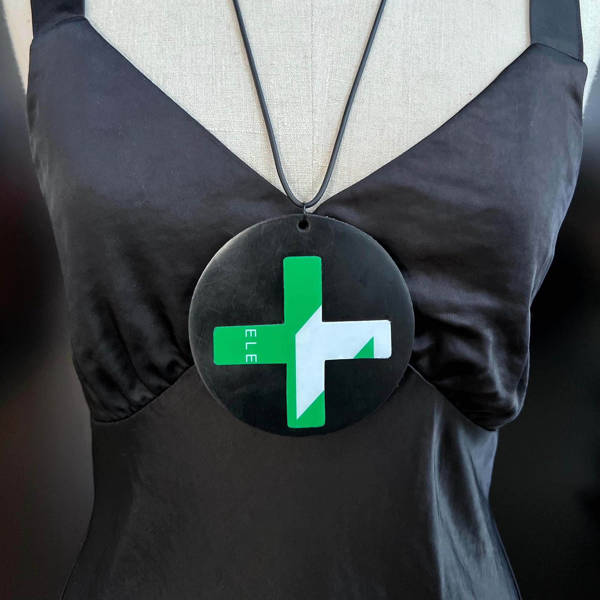 A mannequin wears a large black pendant mounted with a green graphic cross