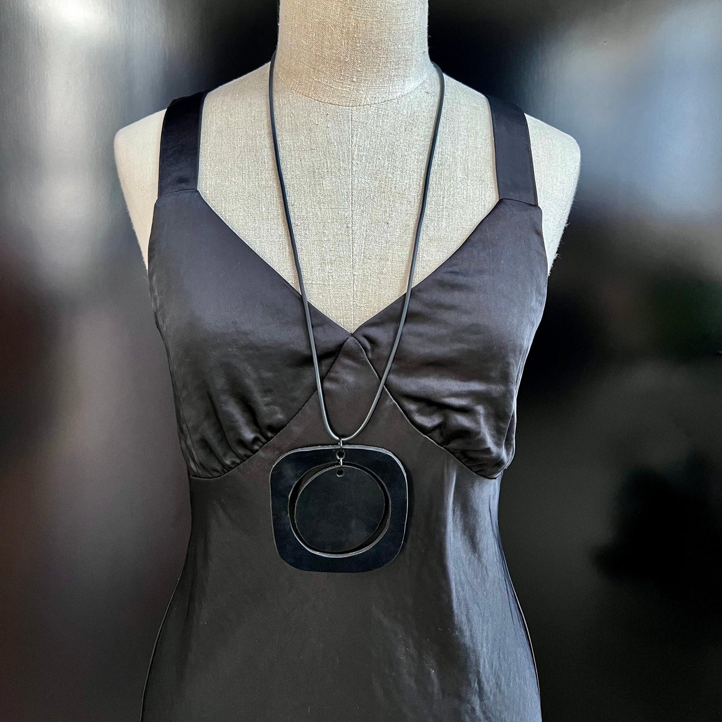 A mannequin wears a rubber black necklace with mid century modern stylings