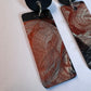 Close up image of a pair of long rectangle earrings with abstract metallic painted surface