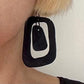 A woman wears an earring of black rubber with a mid century modern style