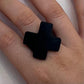 A woman&#39;s finger wearing a small repurposed industrial rubber statement ring in the shape of a cross