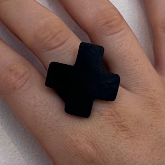 A woman&#39;s finger wearing a small repurposed industrial rubber statement ring in the shape of a cross