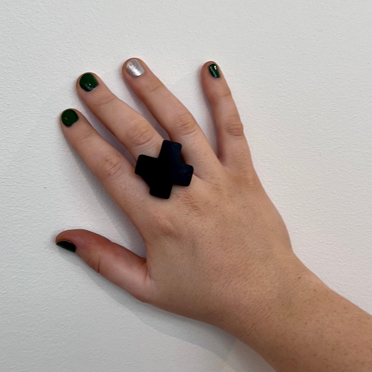 A woman&#39;s hand wearing a small repurposed industrial rubber statement ring in the shape of a cross