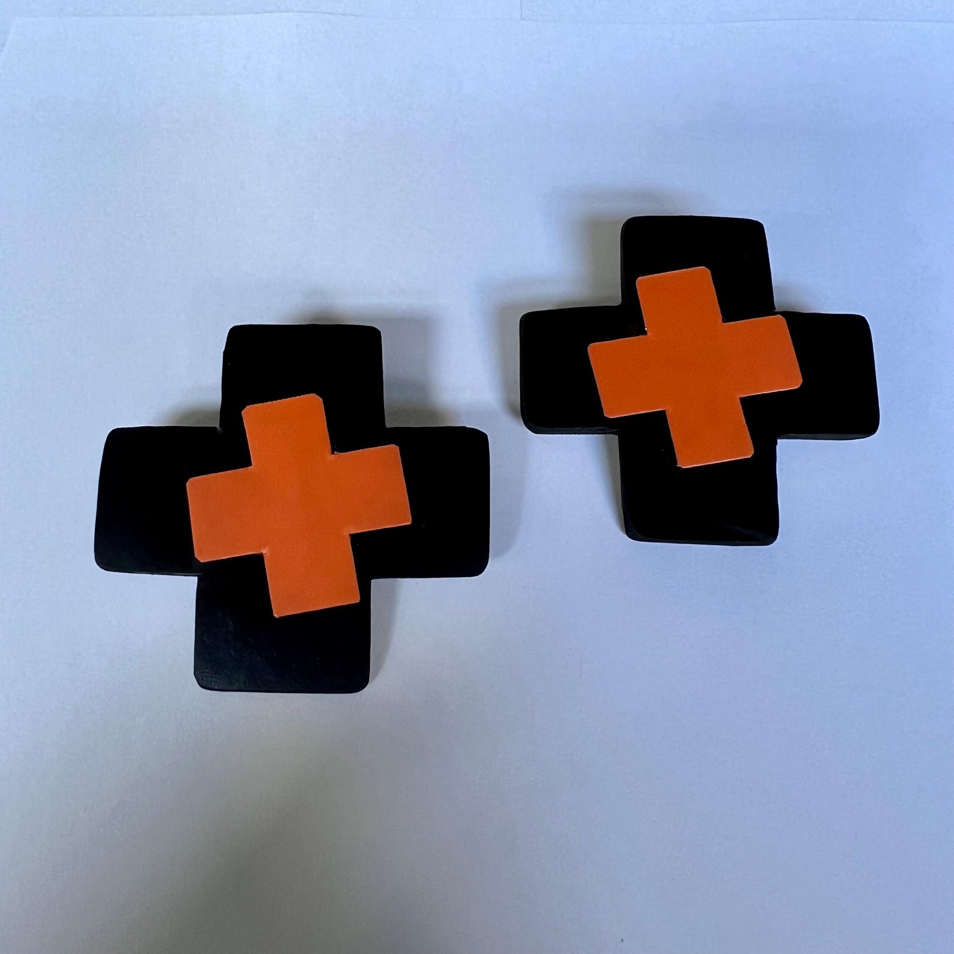 A pair of black rubber cross stud earrings with orange inner crosses