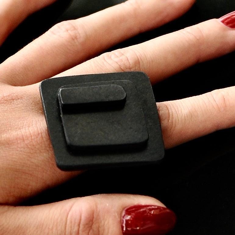 A hand wears a large black rubber ring