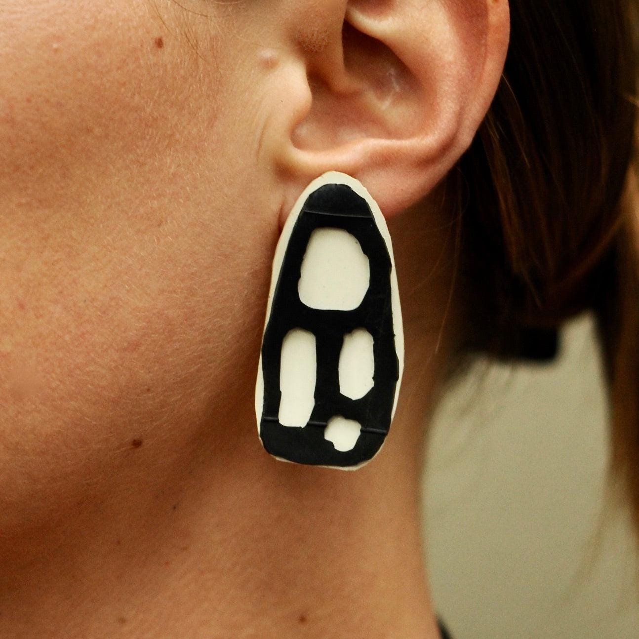 A woman wears Black and white organically shaped 2-layer stud earrings made from repurposed rubber