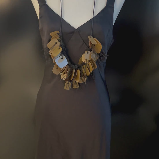 A hand plays with a necklace made from recycle bronze coloured plastic