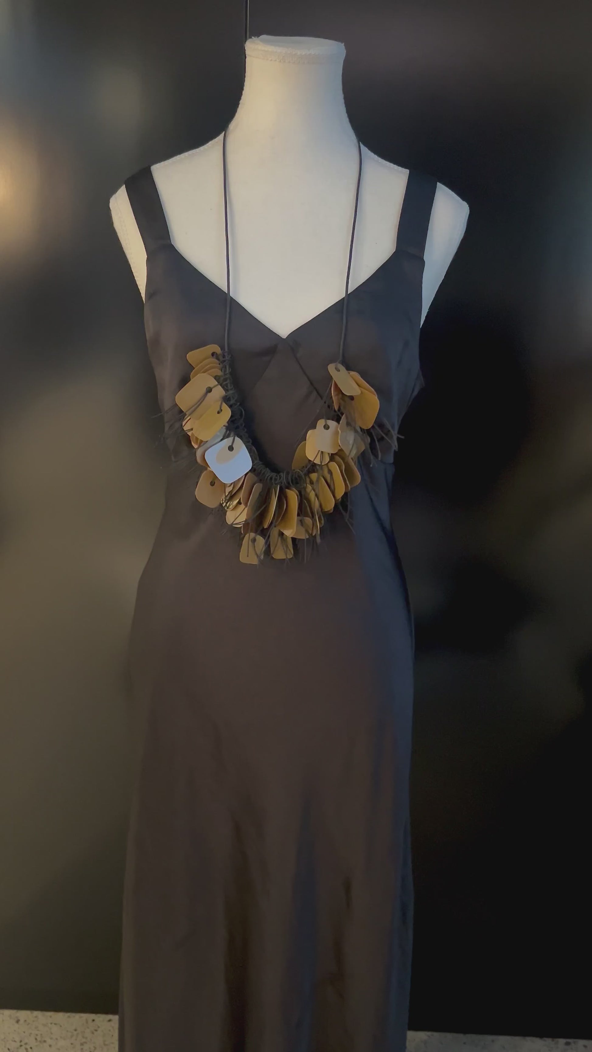 A hand plays with a necklace made from recycle bronze coloured plastic