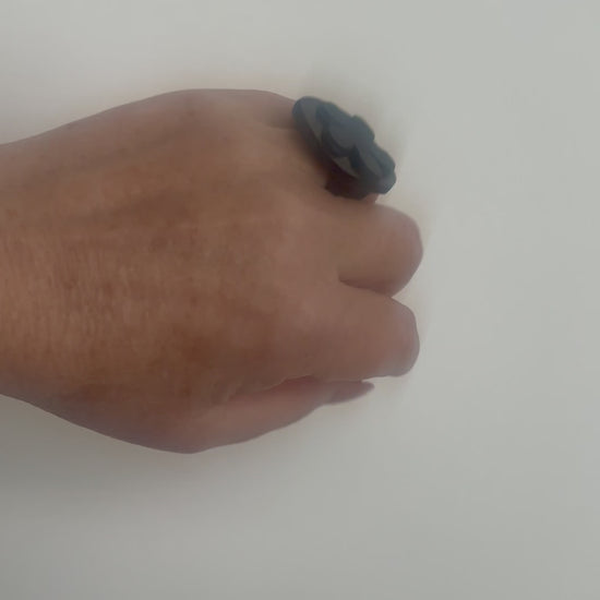 A woman waves her hand and wears a ring topped with a black rubber daisy
