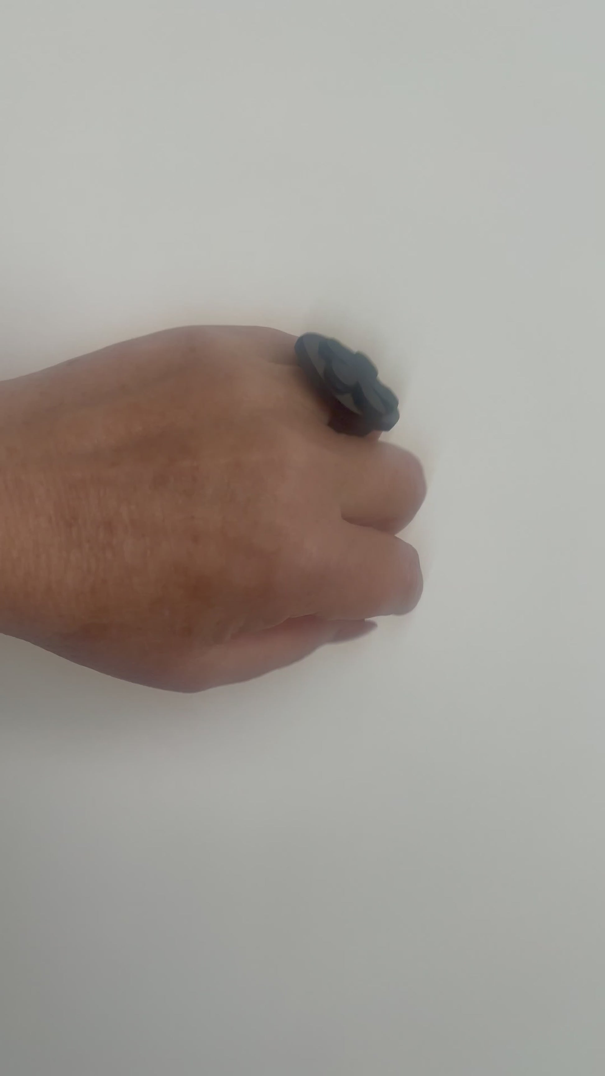 A woman waves her hand and wears a ring topped with a black rubber daisy
