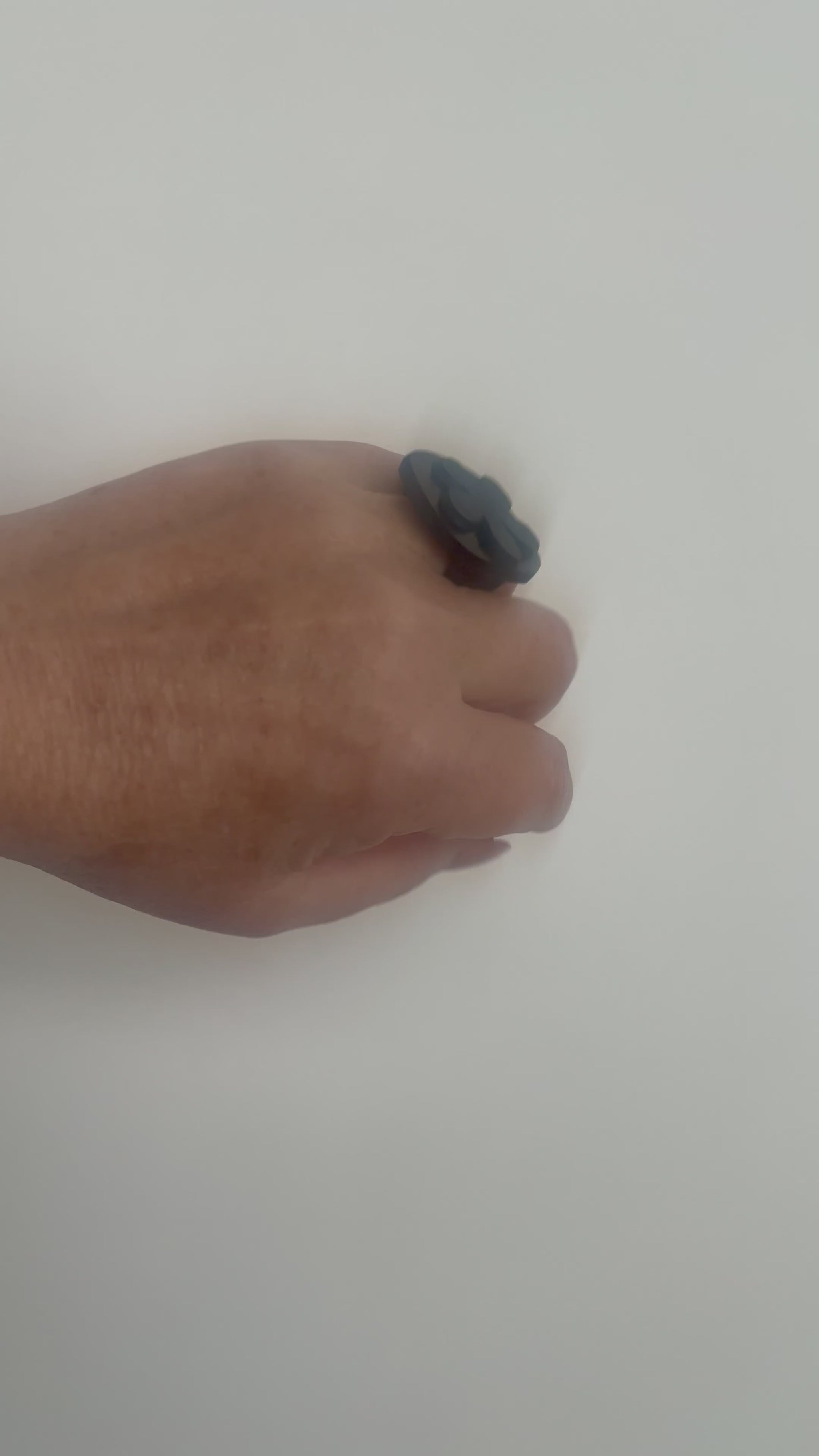 A woman waves her hand and wears a ring topped with a black rubber daisy