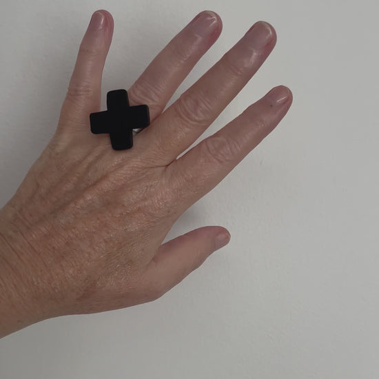 A hand displays a small cross shaped black ring
