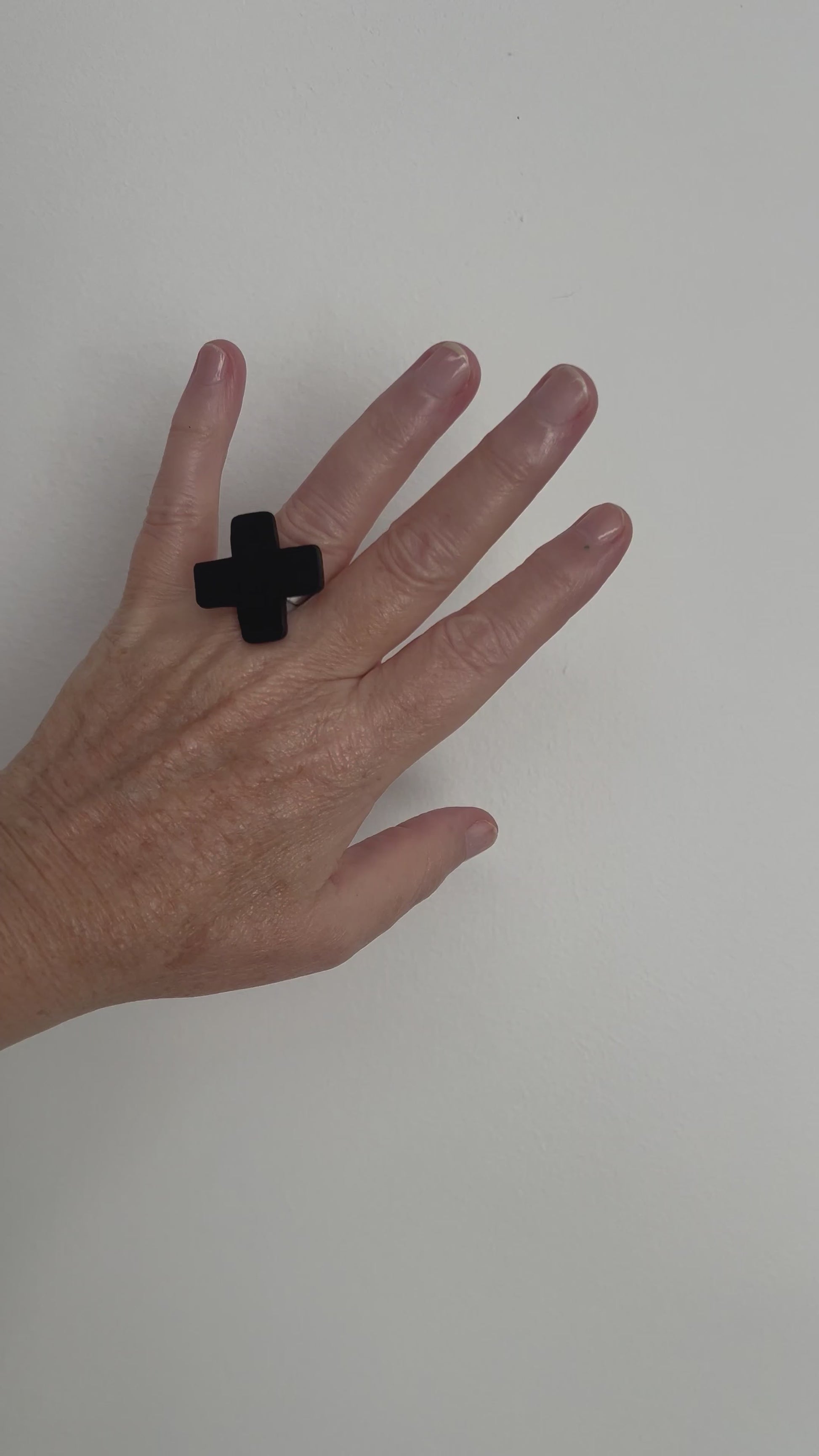 A hand displays a small cross shaped black ring