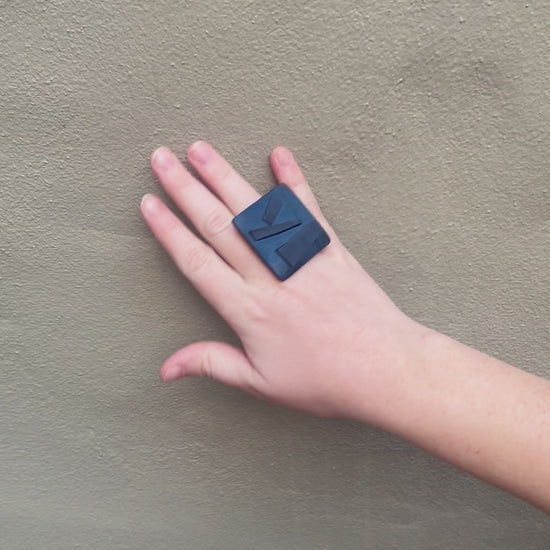 A woman's hand waving and wearing a large black ring tpped with geometric shapes.