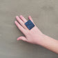 A woman's hand waving and wearing a large black ring tpped with geometric shapes.
