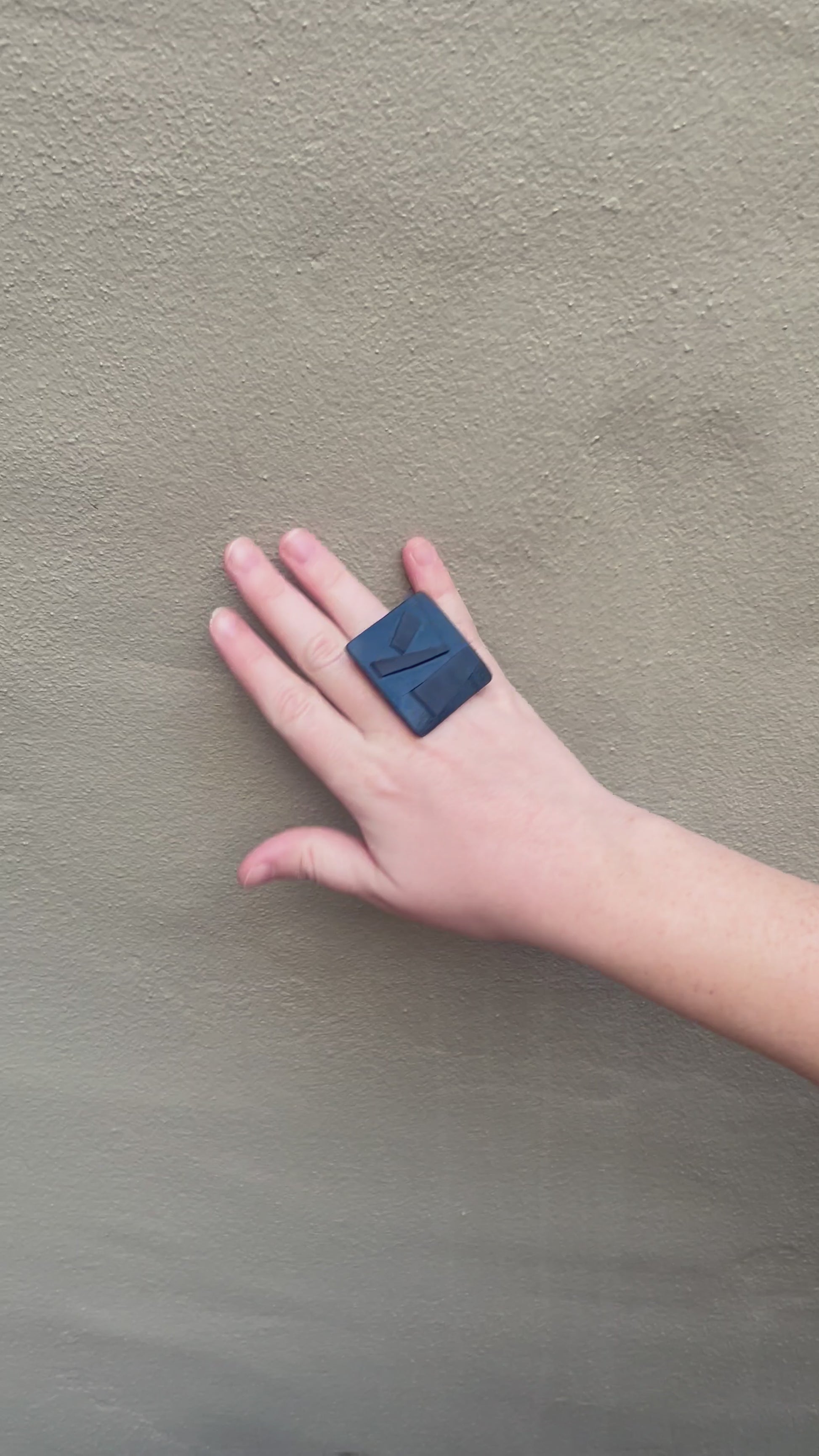 A woman's hand waving and wearing a large black ring tpped with geometric shapes.