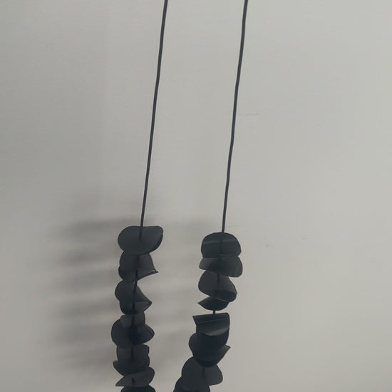 A hand holds a long black necklace