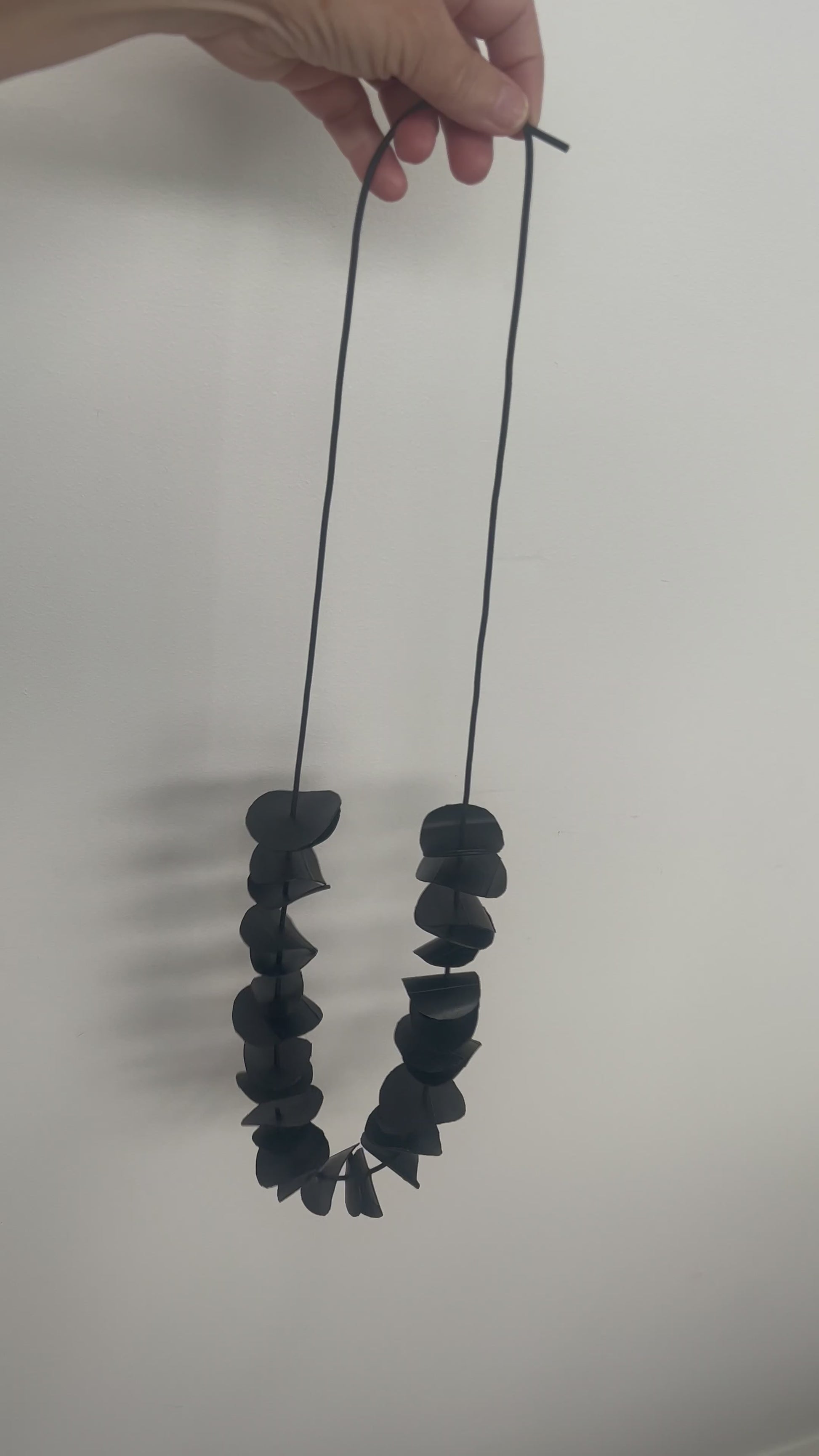 A hand holds a long black necklace
