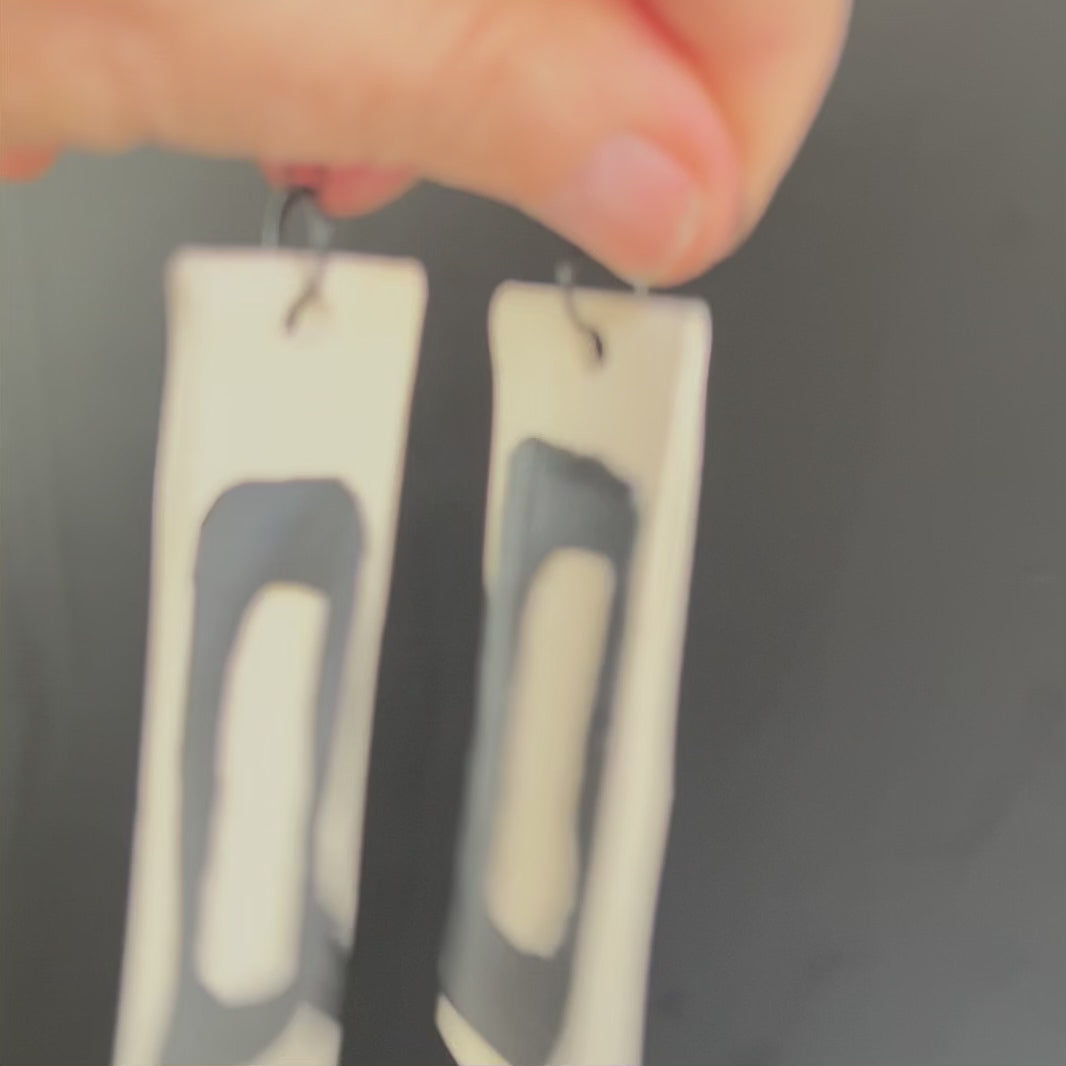 A hand waves a pair of long black and white salvaged rubber earrings