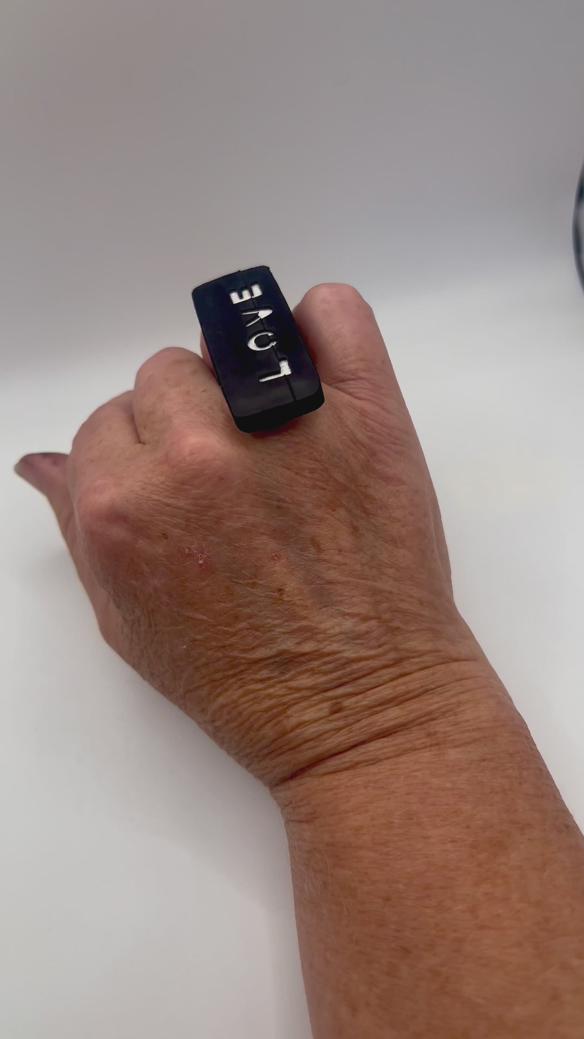 A hand wears a large ring with the word LOVE