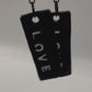 A pair of earrings dangling from a hand with the word LOVE written on them
