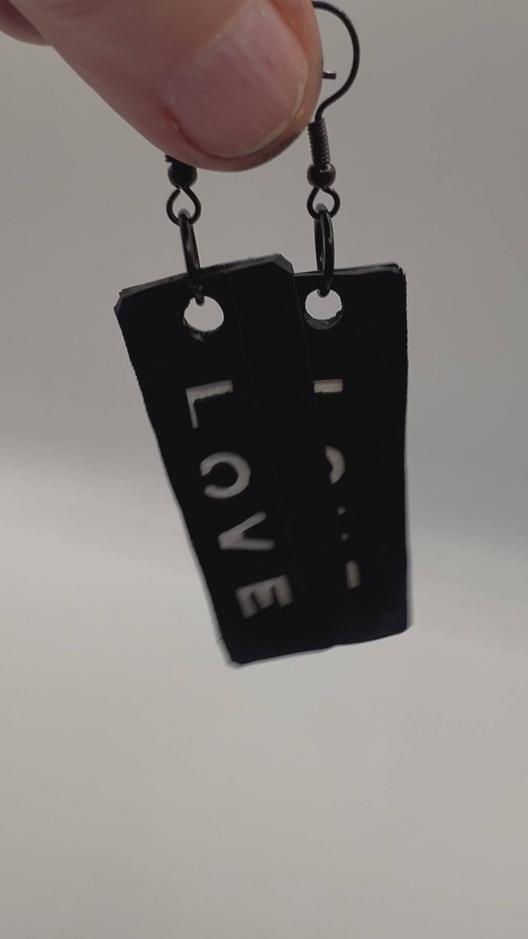 A pair of earrings dangling from a hand with the word LOVE written on them