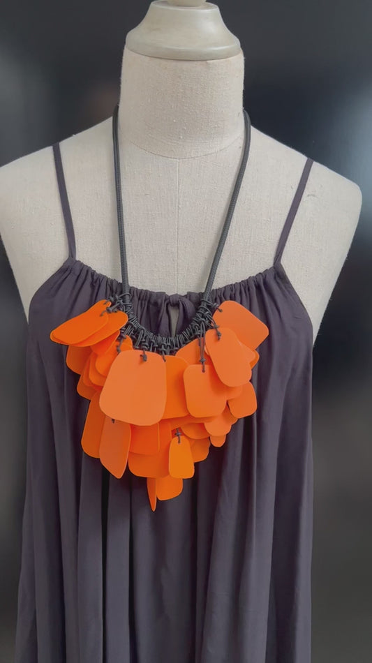 A mannequin wears a necklace of bright orange salvaged plastic