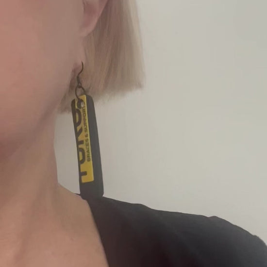 A video of a woman wearing yellow and black plastic and rubber earrings