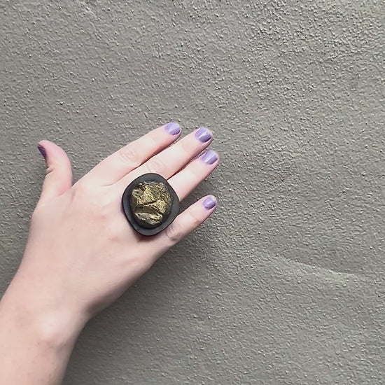 A waving hand wears a black ring topped with a bronze centre