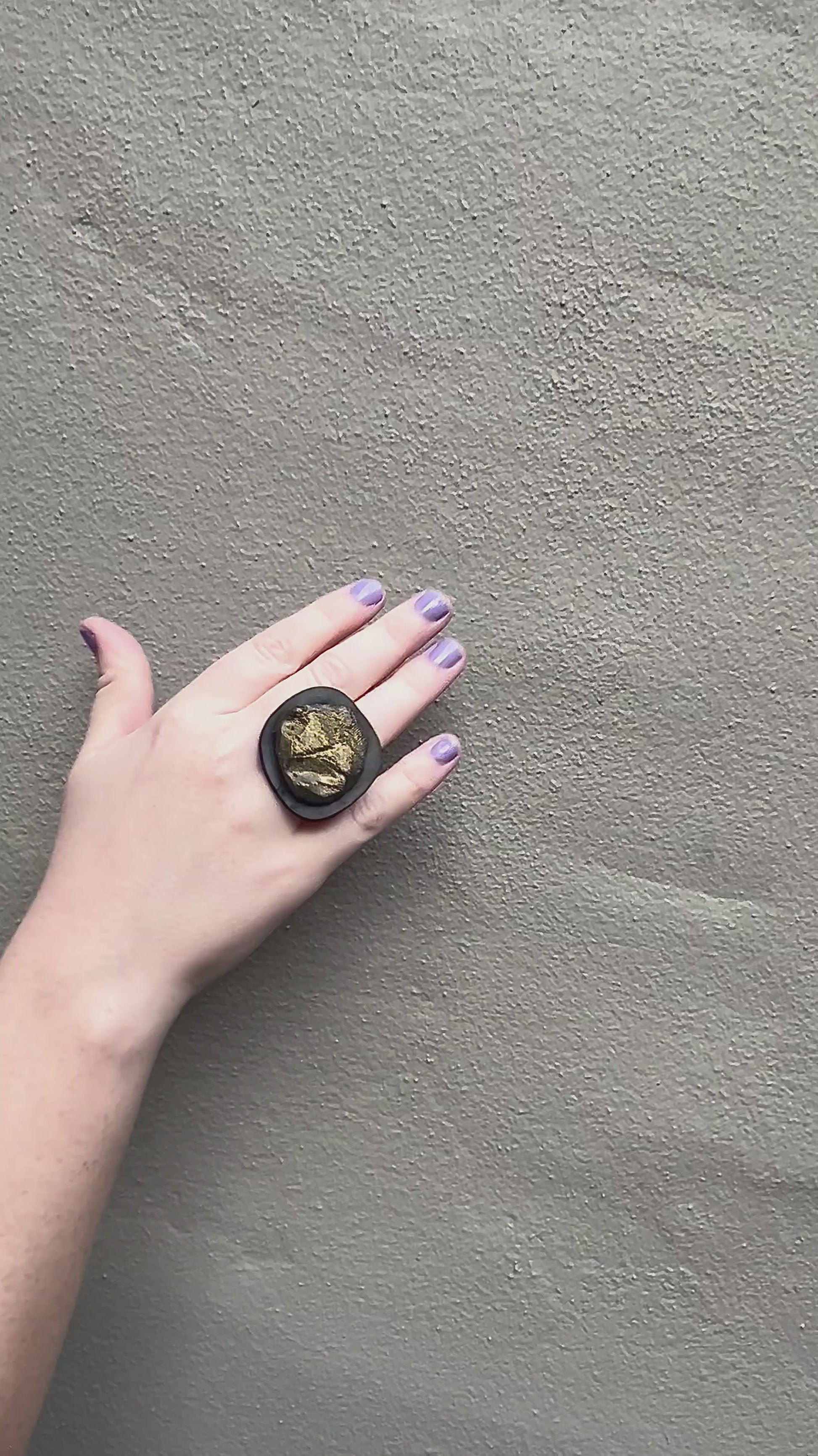A waving hand wears a black ring topped with a bronze centre