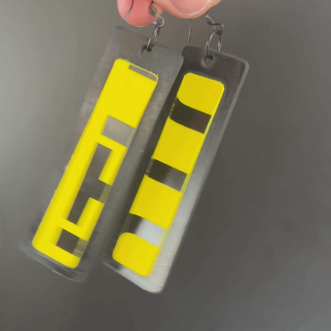 A video shows a hand holding a pair of black and yellow long earrings