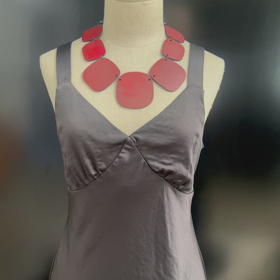 A hand touches a red chunky necklace on a mannequin