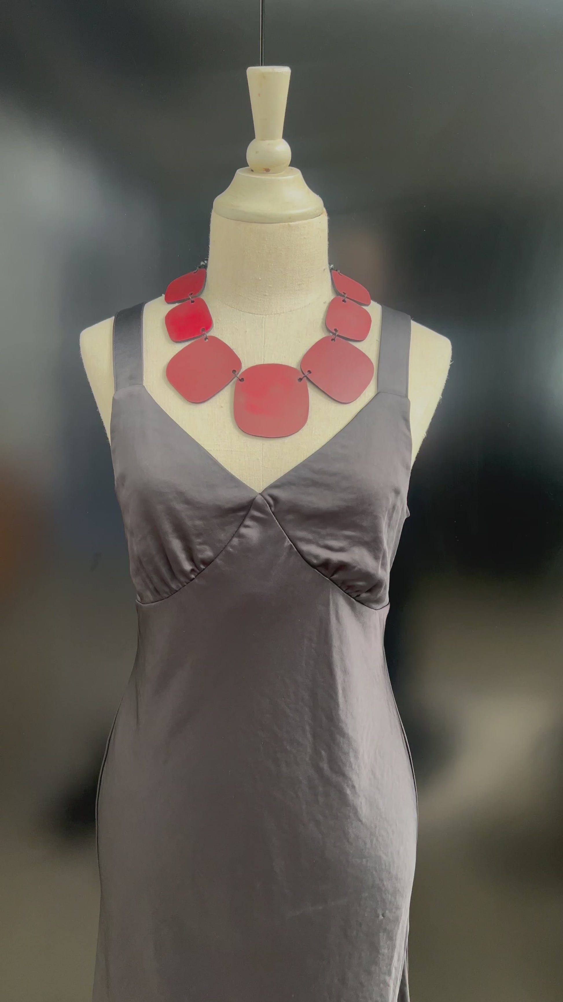 A hand touches a red chunky necklace on a mannequin