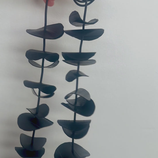 A hand displaces a black rubber necklace shown at a shorter length