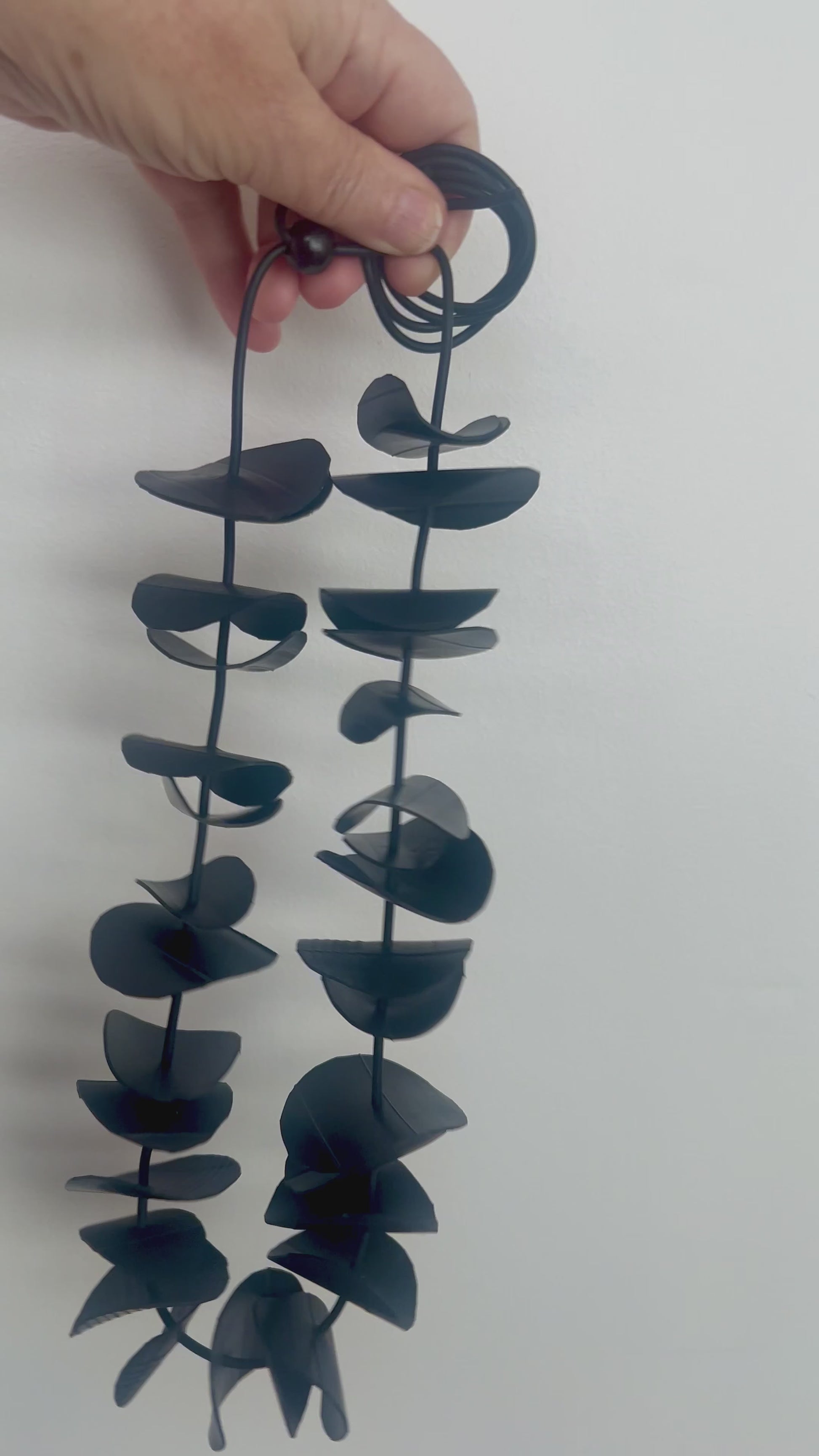 A hand displaces a black rubber necklace shown at a shorter length
