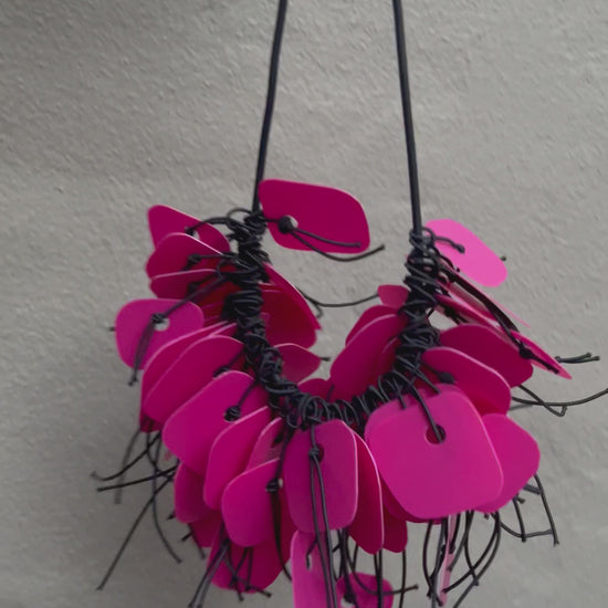 A necklace made from pink coloured recycled plastic spins in the sunlight