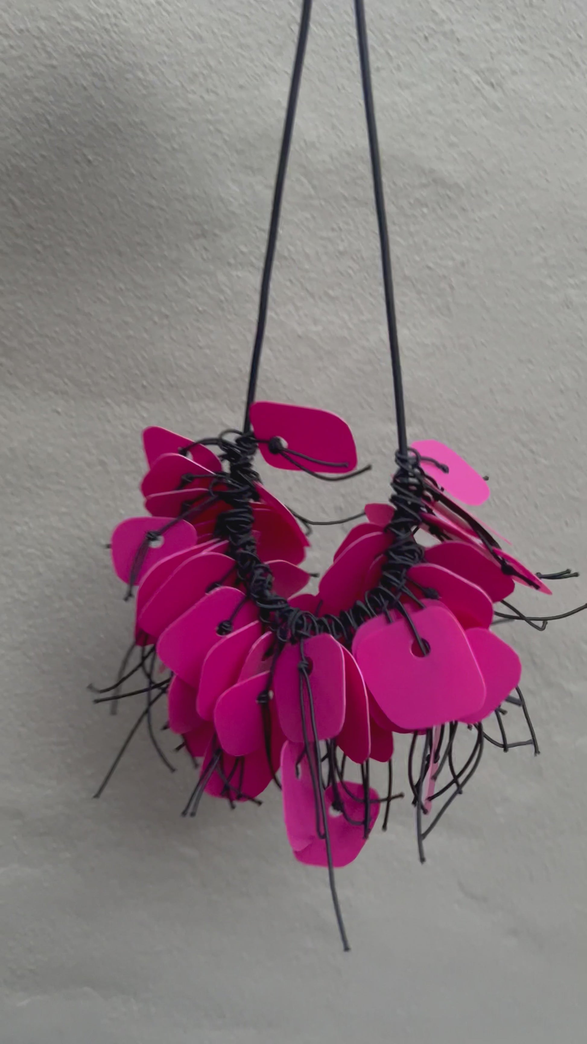 A necklace made from pink coloured recycled plastic spins in the sunlight
