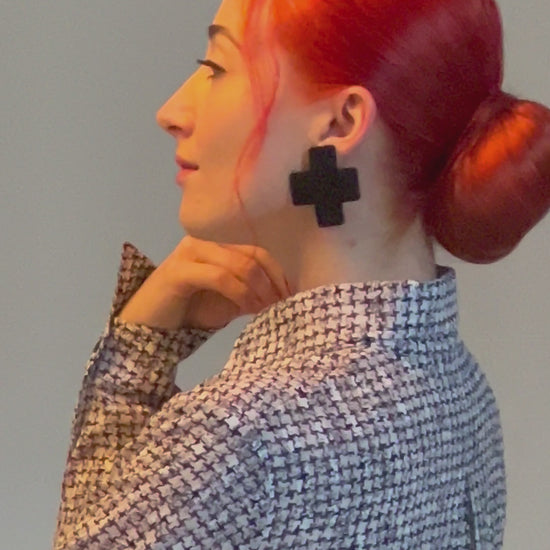 A model wears a pair of black cross stud earrings